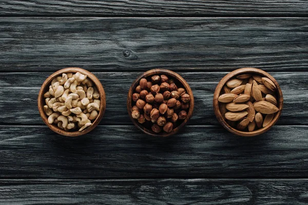 Various nuts in three bowls on dark wooden table — Stock Photo