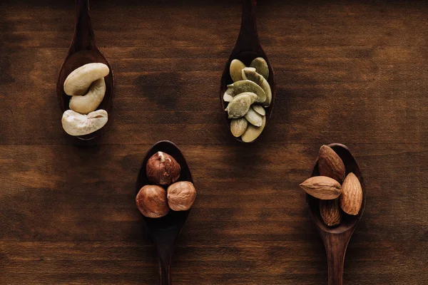 Variety of nuts in dark spoons on wooden surface — Stock Photo