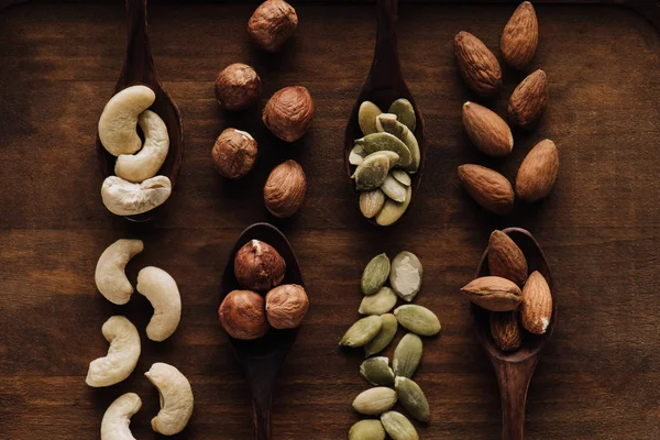 Mixed nuts in dark spoons on wooden tabletop — Stock Photo