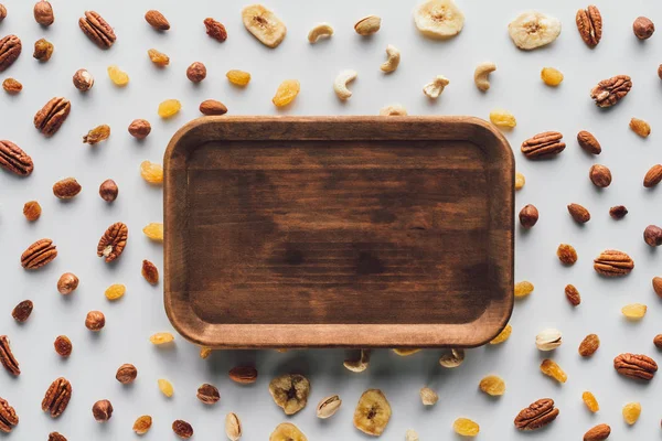 Flat lay with dried fruits and nuts with wooden plate in center isolated on white background — Stock Photo