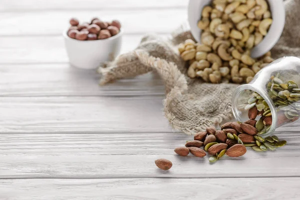 Sabrosos frutos secos en cuencos de cerámica y vidrio sobre mesa de madera blanca - foto de stock