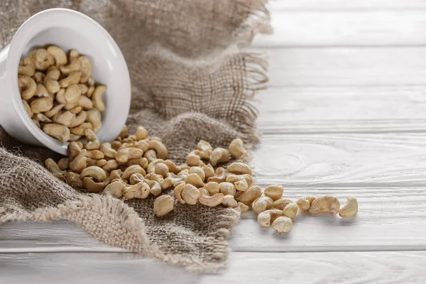 Anacardo en tazón de cerámica blanca sobre tela de saco y mesa de madera blanca - foto de stock