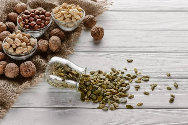 Various nuts in glass bowls and pumpkin seeds in jar on white wooden surface — Stock Photo