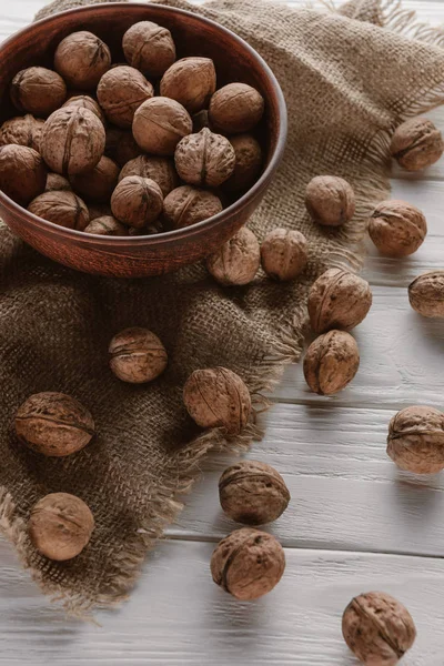 Walnuts in wooden bowl with sackcloth on white wooden table — Stock Photo