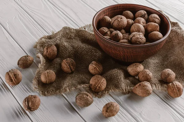 Walnuts with wooden bowl and sackcloth on white wooden background — Stock Photo