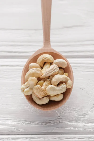 Handful of cashew in wooden spoon on white wooden surface — Stock Photo