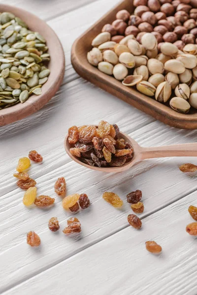 Mixed nuts in plates and raisins in spoon on white wooden table — Stock Photo