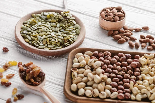 Assortiment de délicieuses noix et raisins secs dans des assiettes en bois et une cuillère — Photo de stock