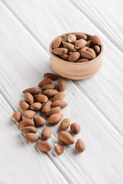 Délicieuses amandes dans un bol en bois sur fond blanc en bois — Photo de stock