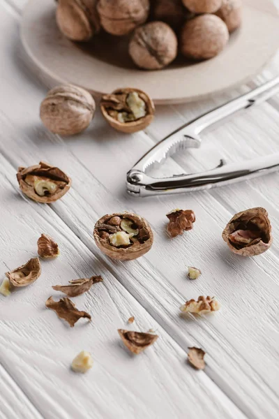 Walnuts with metal nutcracker on white wooden surface — Stock Photo