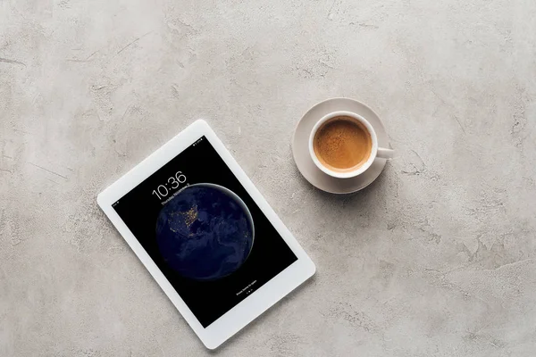 Vista superior de la taza de café y tableta con pantalla de bloqueo ios en la superficie de hormigón - foto de stock