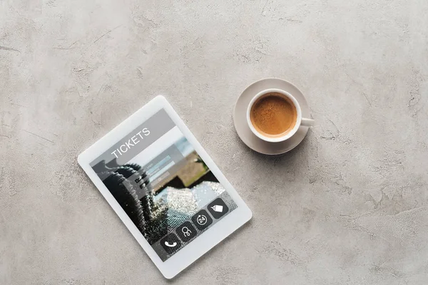 Top view of cup of coffee and tablet with tickets app on screen on concrete surface — Stock Photo