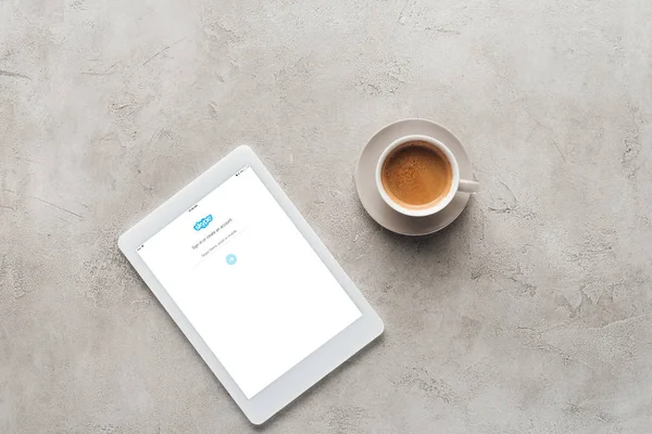 Draufsicht auf Tasse Kaffee und Tablet mit Skype-App auf dem Bildschirm auf Betonoberfläche — Stockfoto