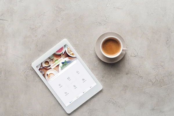 Vista superior de la taza de café y tableta con aplicación cuadrada en la pantalla en la superficie de hormigón - foto de stock