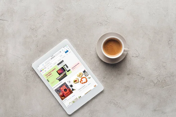 Draufsicht auf Tasse Kaffee und Tablet mit ebay-Website auf dem Bildschirm auf Betonoberfläche — Stockfoto