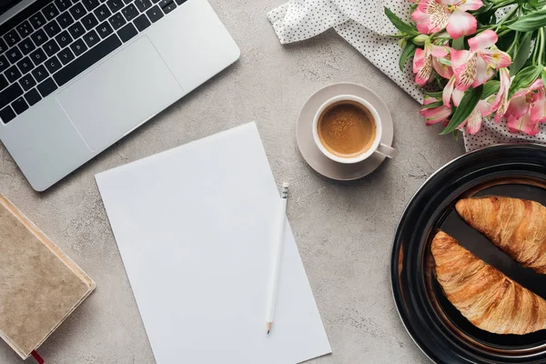 Vista superior de la taza de café con papel en blanco, croissants y portátil en la superficie de hormigón - foto de stock