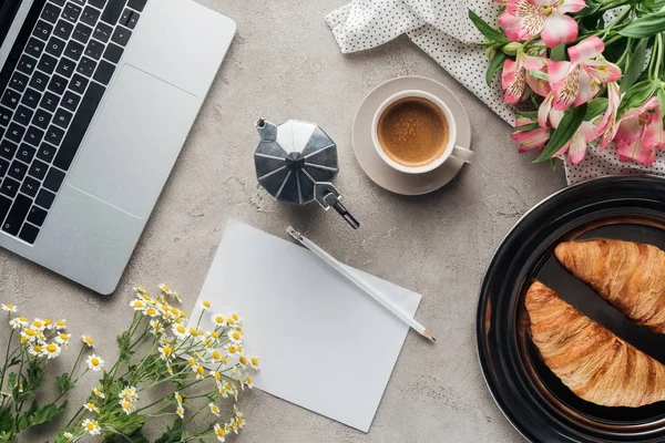 Vista superior de xícara de café com papel em branco, croissants e flores na superfície de concreto — Fotografia de Stock