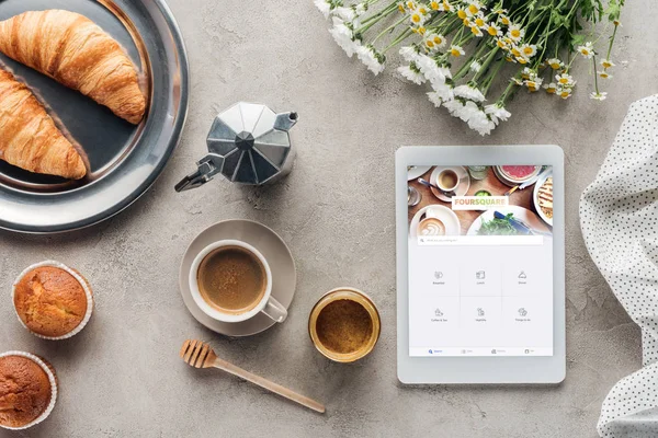 Kaffee mit Gebäck und Tablet mit Foursquare-App auf dem Bildschirm auf Betonoberfläche — Stockfoto