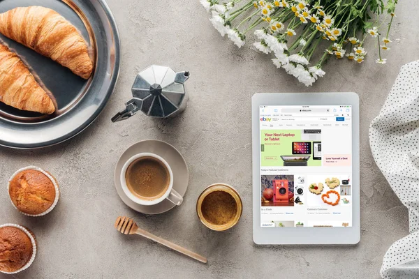 Draufsicht auf Kaffee mit Gebäck und Tablet mit ebay-Website auf dem Bildschirm auf Betonoberfläche — Stockfoto