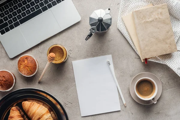 Top view of coffee with sweet pastry, laptop and blank paper on concrete surface — Stock Photo