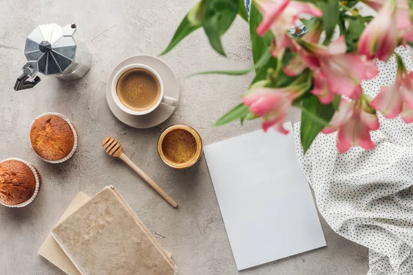 Blick von oben auf köstlichen Kaffee mit Muffins, leerem Papier und Alstroemeria-Bouquet auf Betonoberfläche — Stockfoto