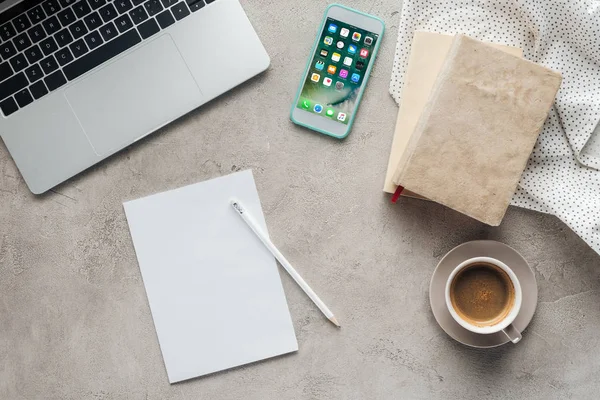 Vue du haut du café avec ordinateur portable et smartphone avec application écran d'accueil ios à l'écran sur une surface en béton avec du papier blanc — Photo de stock