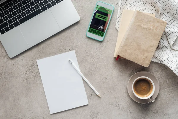 Vista superior de café com laptop e smartphone com aplicativo de reserva na tela na superfície de concreto com papel em branco — Fotografia de Stock