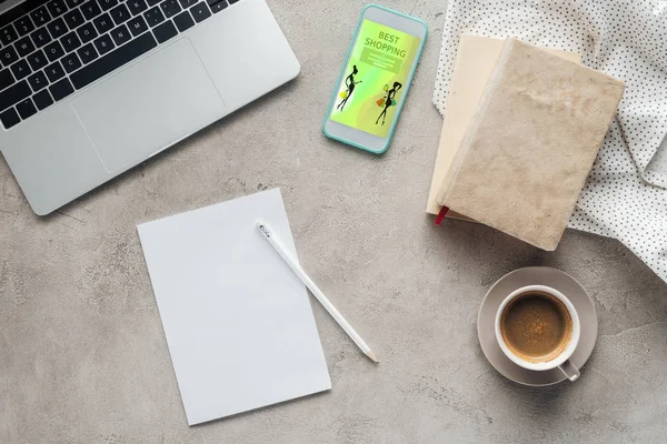 Top view of coffee with laptop and smartphone with best shopping app on screen on concrete surface with blank paper — Stock Photo