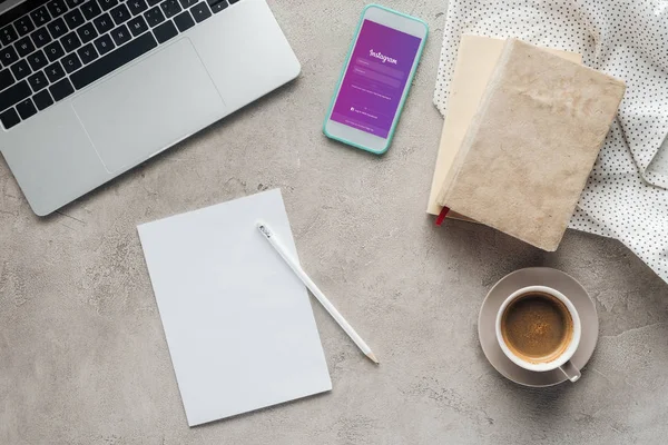 Vue du haut du café avec ordinateur portable et smartphone avec application instagram à l'écran sur une surface en béton avec papier blanc — Photo de stock