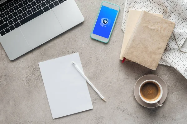 Ansicht von Kaffee mit Laptop und Smartphone mit Shazam-App auf dem Bildschirm auf Betonoberfläche mit leerem Papier — Stockfoto