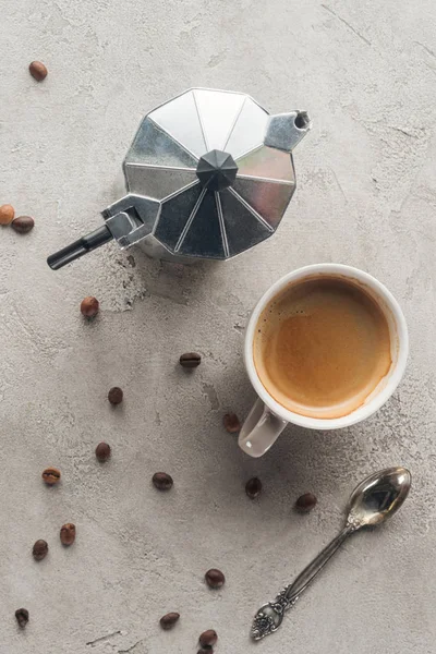 Vista superior da xícara de café delicioso e panela de moka na superfície de concreto com grãos de café derramados — Fotografia de Stock