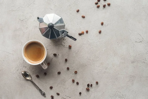 Top view of cup of coffee and moka pot on concrete surface with spilled coffee beans — Stock Photo