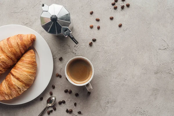 Vue de dessus de tasse de café avec croissants et pot de moka sur la surface en béton avec grains de café renversés — Photo de stock