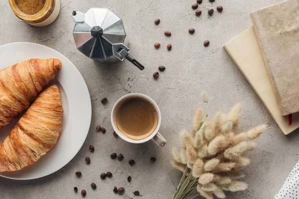 Vue du dessus de tasse de café avec croissants et pot de moka sur la surface en béton avec bouquet lagurus ovatus et livre — Photo de stock