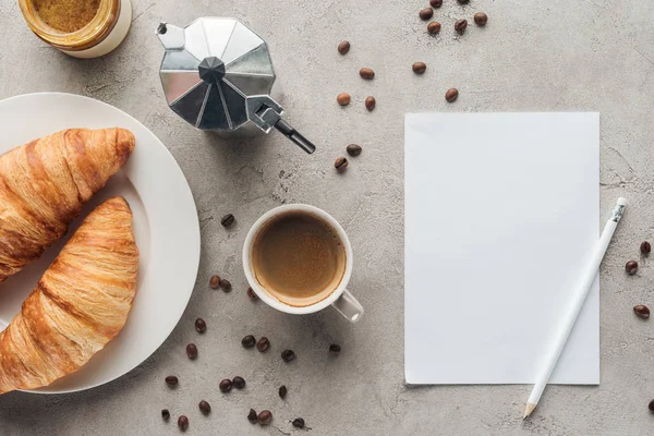 Vista superior de la taza de delicioso café con croissants y papel en blanco en la superficie de hormigón - foto de stock