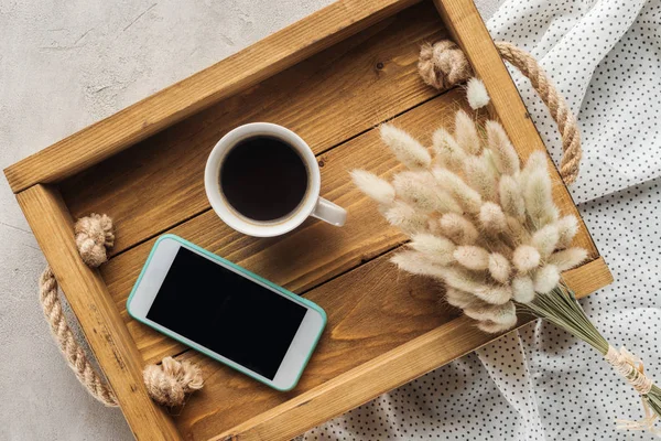 Top view of cup of coffee and smartphone with blank screen on tray with lagurus ovatus bouquet on concrete surface — Stock Photo
