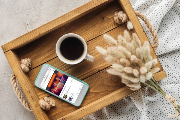 Vista superior de la taza de café y teléfono inteligente con sitio web soundcloud en la pantalla en bandeja con ramo de lagurus ovatus en la superficie de hormigón - foto de stock