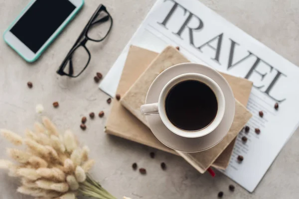 Vista superior da xícara de café em pé sobre livros e jornal com inscrição de viagem na superfície de concreto — Fotografia de Stock