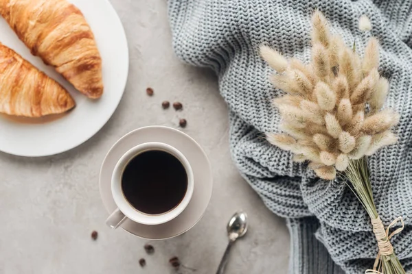 Top view of cup of coffee with croissants and on lagurus ovatus bouquet concrete surface — Stock Photo