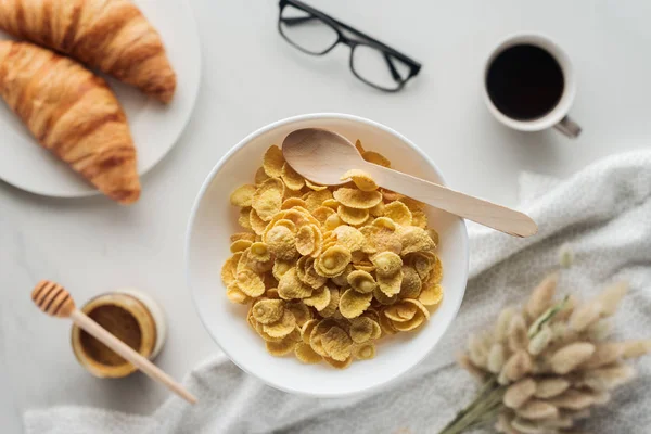 Vue du dessus du bol de céréales sèches avec délicieux café, croissants et lagurus ovatus bouquet sur blanc — Photo de stock