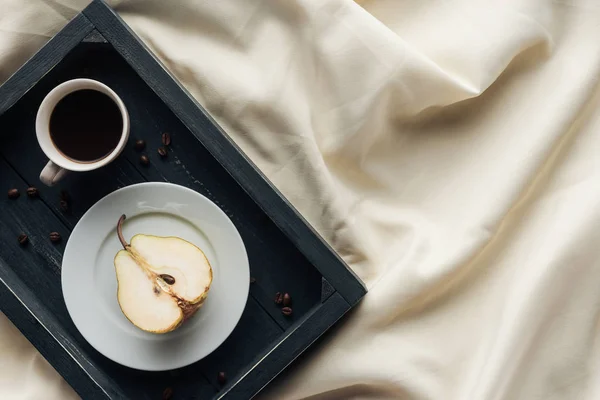 Vista superior da xícara de café com metade de pêra madura em pano bege, café da manhã no conceito de cama — Fotografia de Stock