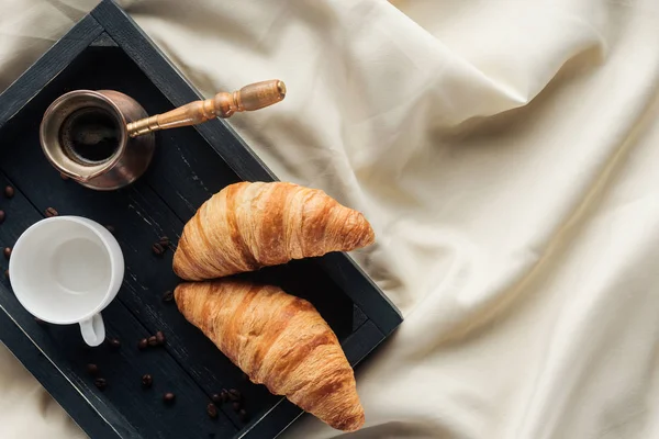 Vista dall'alto di caffè e croissant su vassoio su stoffa beige, colazione a letto concetto — Foto stock