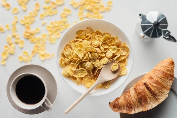 Vista superior del tazón de maíz hojuelas desayuno con taza de café y croissant en blanco - foto de stock