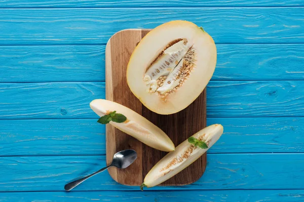 Vista superior de melão fatiado maduro doce com hortelã e colher na placa de corte na superfície de madeira azul — Fotografia de Stock