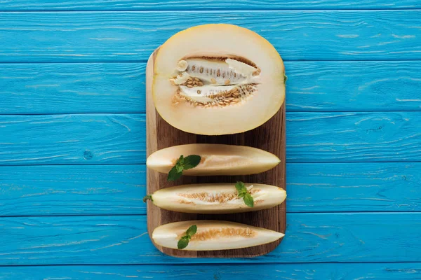 Vue de dessus du melon tranché mûr sucré sur la planche à découper sur une surface en bois bleue — Photo de stock