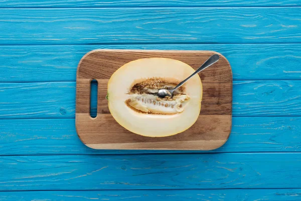 Draufsicht auf süße reife Melone mit Löffel auf Schneidebrett auf blauer Holzoberfläche — Stockfoto