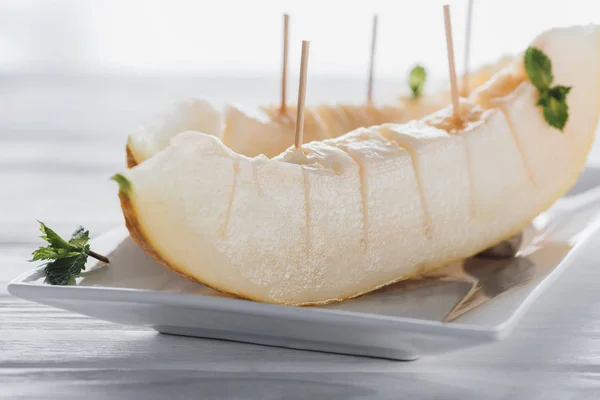 Крупным планом вид нарезанной сладкой спелой дыни с мятой на тарелке — стоковое фото
