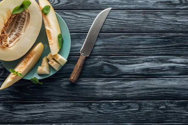 Top view of sweet ripe melon with mint on plate and knife on wooden surface — Stock Photo