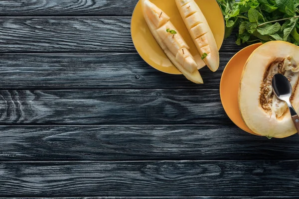 Süße reife Melone mit Löffel auf gelben Tellern und frischer Minze auf Holzoberfläche — Stockfoto