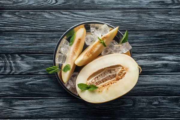Vista superior de melón maduro dulce con menta y cubitos de hielo en la superficie de madera - foto de stock